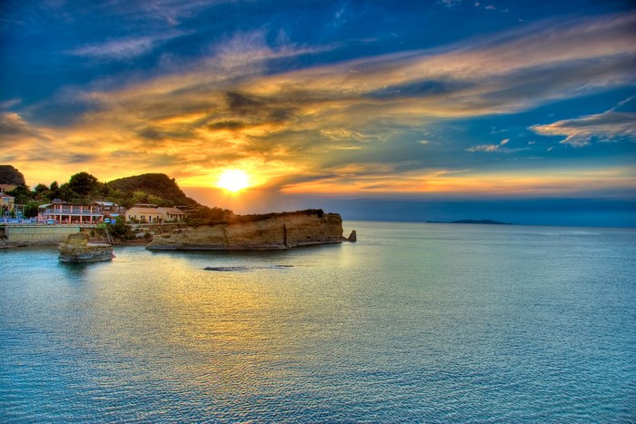 Sunset over the sea with cliffs and buildings on Corfu island, Greece