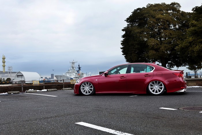 Red Lexus LS460 with custom wheels parked by a harbor