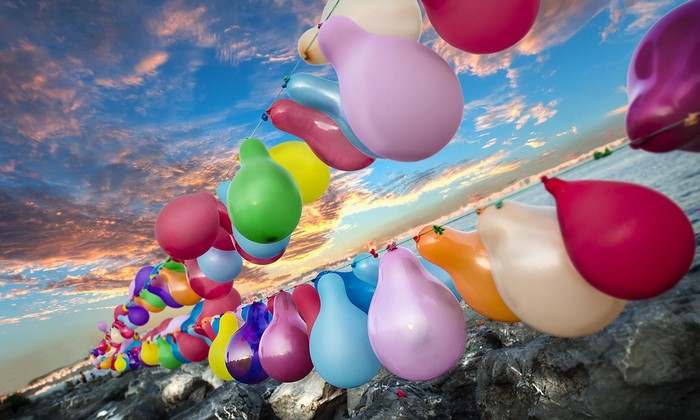 Colorful balloons strung along a rocky shore with a sunset sky