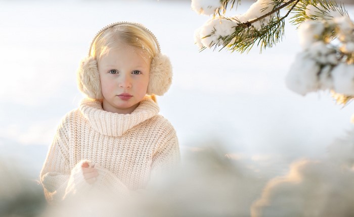 Little girl in a sweater and earmuffs in the snow
