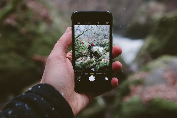 Person taking photo of hiker by waterfall with iPhone