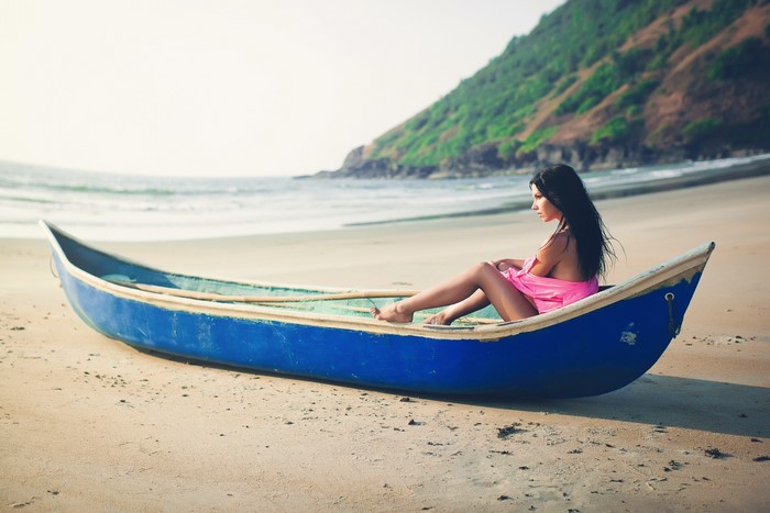 Woman in pink dress sitting in a blue boat on a beach