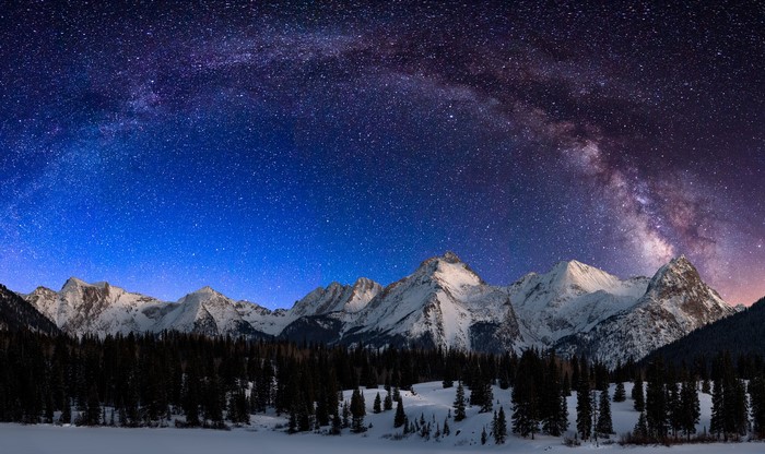 Milky Way over snow-capped mountains and pine forest