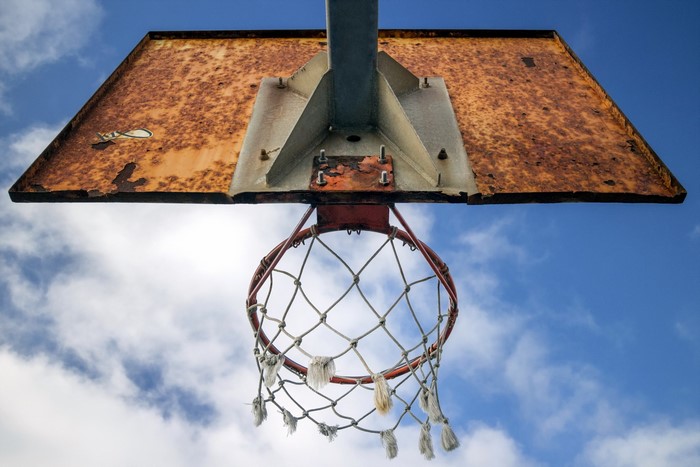 Rusty basketball hoop and backboard against blue sky