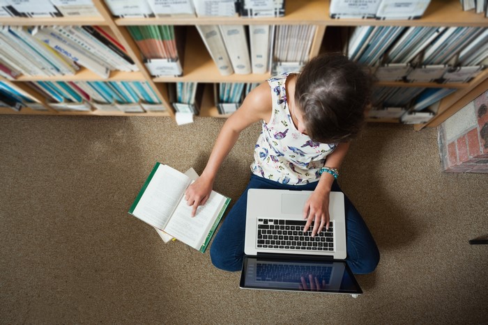 Girl studying with laptop and book in library