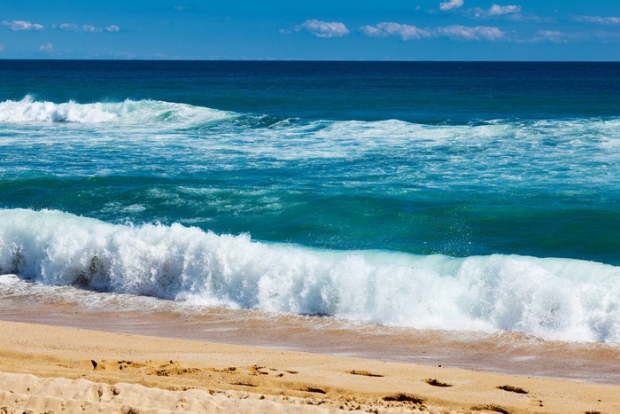 Waves crashing on a sandy beach under a blue sky