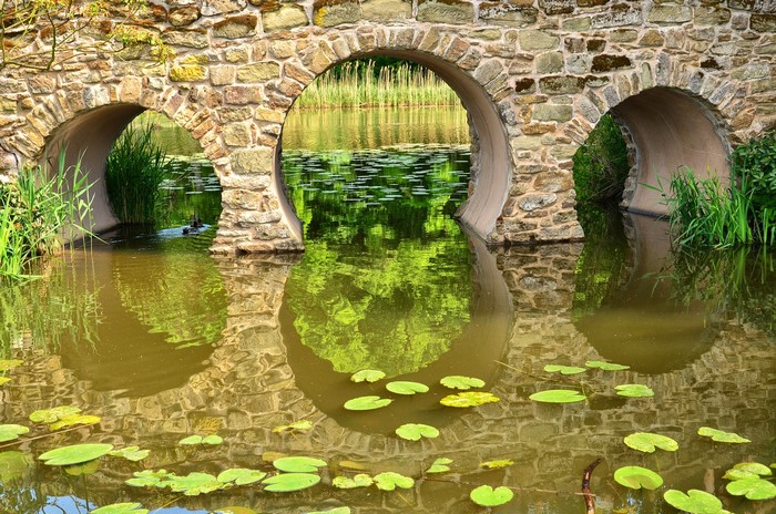 Stone bridge with arches over a pond with lily pads
