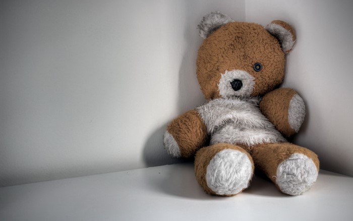 A worn teddy bear sits in a corner