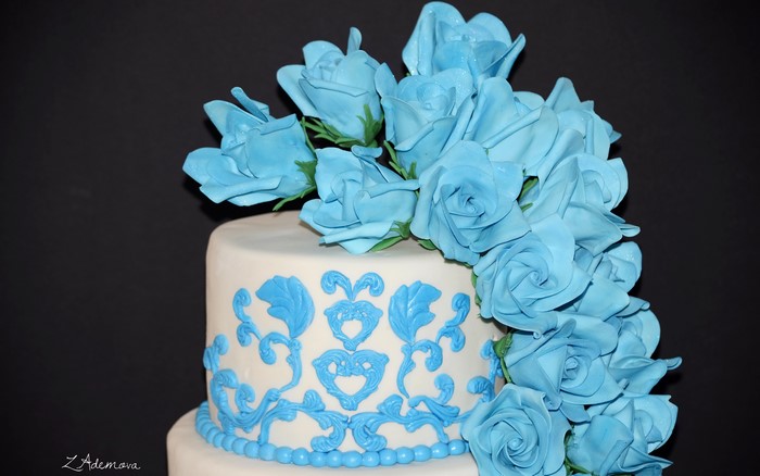 White cake with blue roses and ornate icing