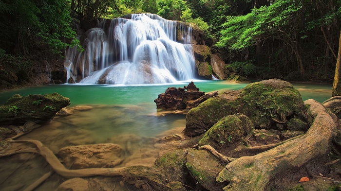 A cascading waterfall flows into a turquoise pool surrounded by lush green forest.