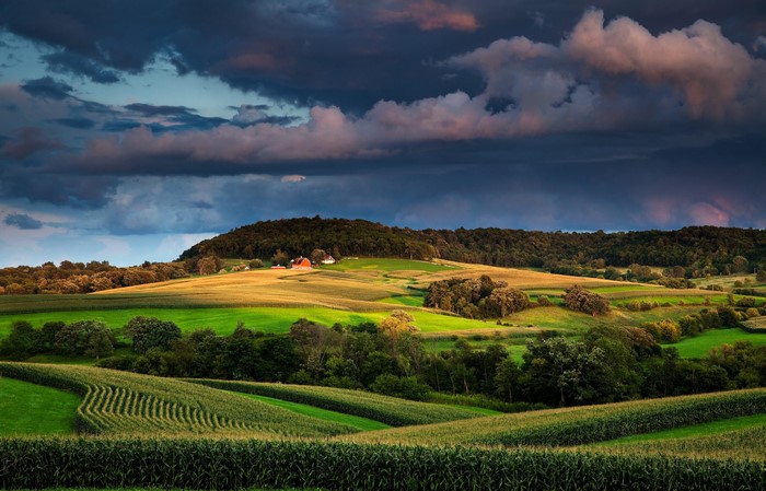 Farm fields and rolling hills under stormy sky