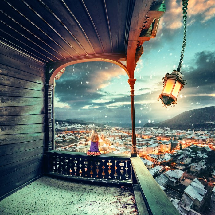 Girl on balcony overlooking snowy town at dusk