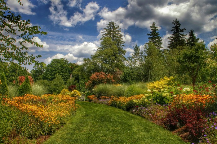 A winding garden path with colorful flowers and trees under a cloudy sky