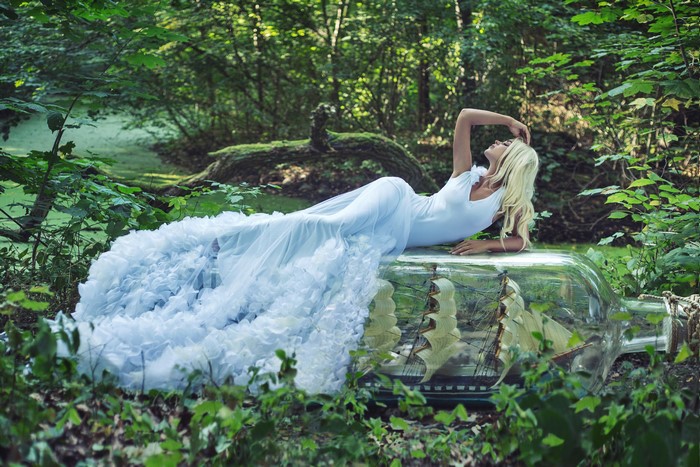 Blonde girl in white dress lying on a bottle with a ship inside