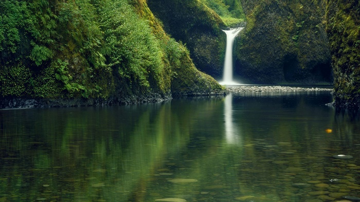 Waterfall cascading into a clear river in a mossy gorge