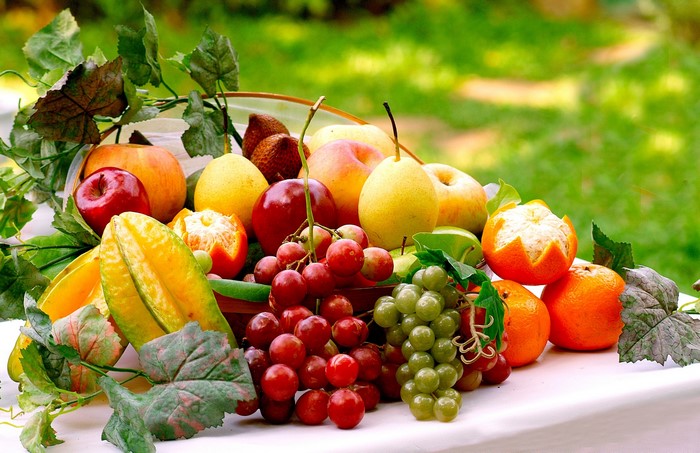 A fruit basket with grapes, pears, apples, and oranges