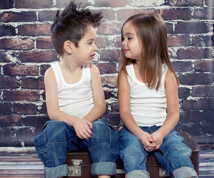 Boy and girl in jeans and white tank tops sitting on a suitcase