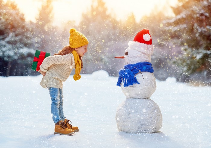 Girl with Gift Next to Snowman in Winter
