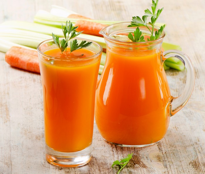Carrot juice in a glass and pitcher with celery and carrots