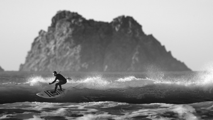Surfer on a wave with a rocky island in the background
