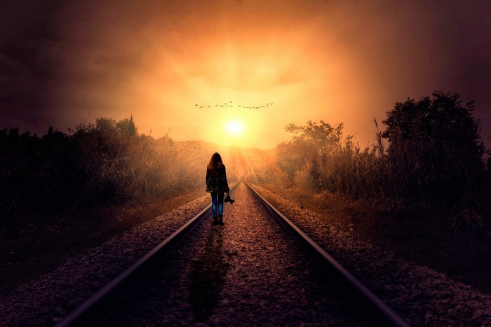 Woman walking on railroad tracks at sunset