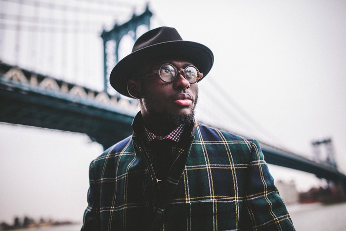 Man in Hat and Plaid Jacket near Bridge