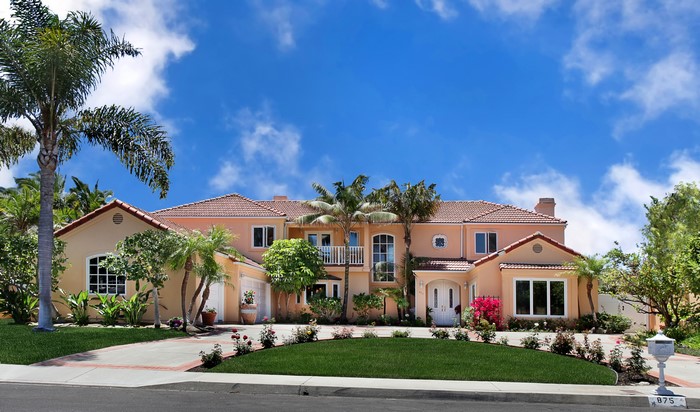 Large peach-colored mansion with palm trees and a blue sky