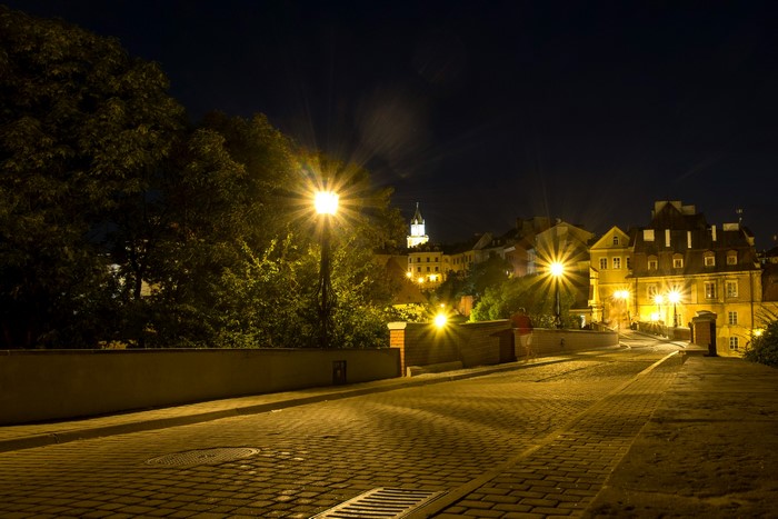 Street lights illuminate a cobblestone road in Lublin, Poland at night.