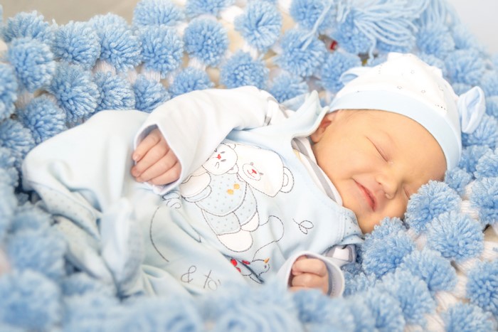 Newborn baby sleeping in a blue pom-pom blanket