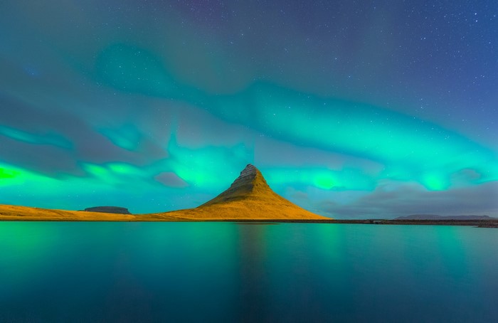 Kirkjufell mountain and Aurora Borealis over water in Iceland