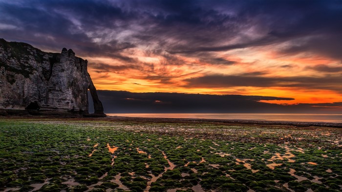 Dramatic sunset over a rocky coast with mossy foreground