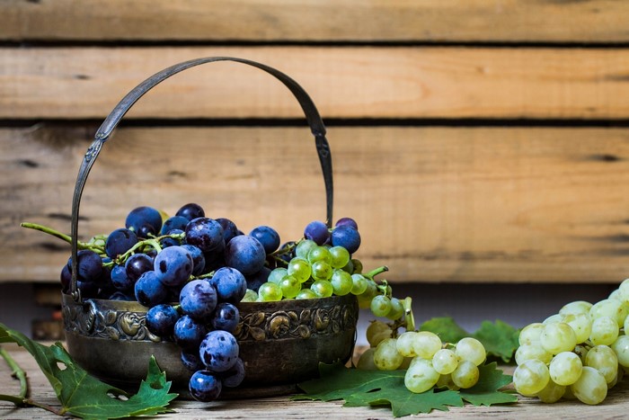 Grapes in a decorative metal basket on a wooden surface
