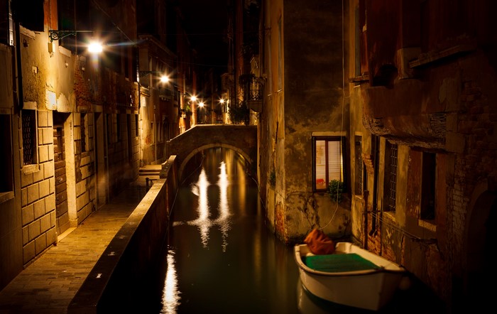 Venice canal at night with a boat and bridge