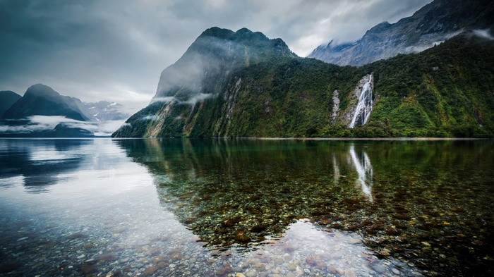 Waterfall cascading down a misty mountain into a clear lake