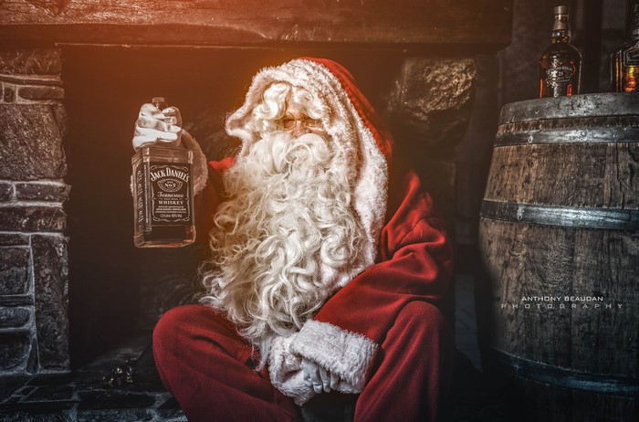 Santa Claus holding Jack Daniel's bottle by fireplace