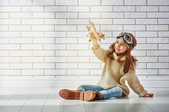 Little girl in sweater and winter hat holding airplane