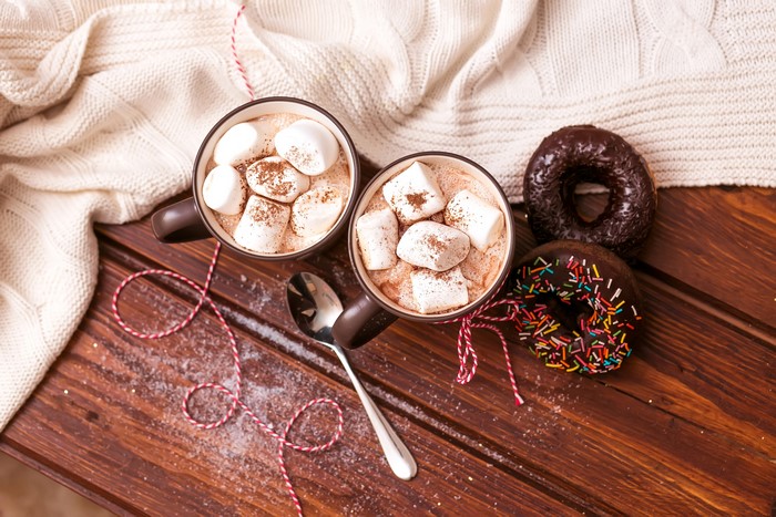 Two cups of hot chocolate with marshmallows and donuts