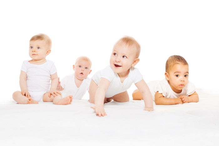 Four babies in white onesies on a white background
