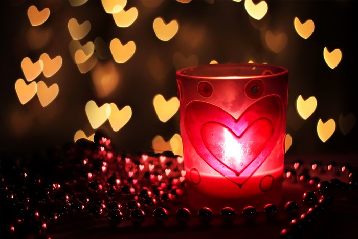 Candle in a heart-decorated glass with heart bokeh