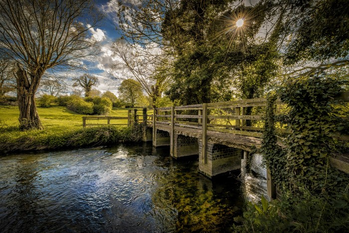 Wooden bridge over a river with sun rays