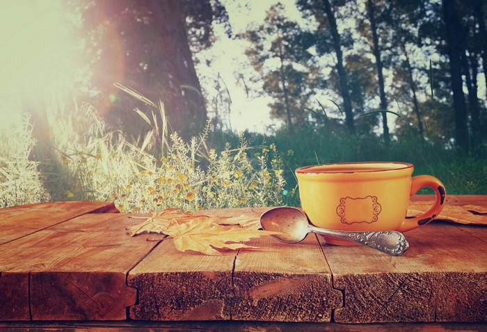 Cup and spoon on a wooden table with autumn leaves