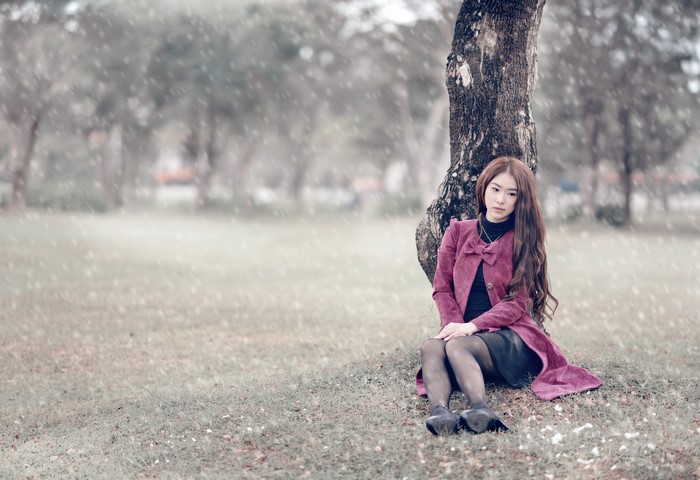 Asian woman sitting by a tree in a park