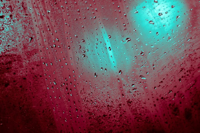 Water drops on a textured surface with red and teal lighting