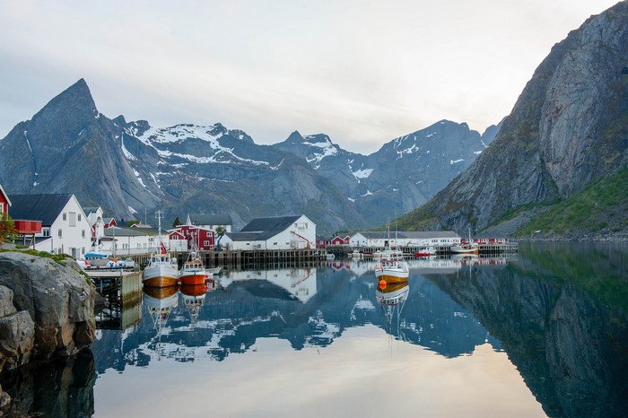 Fishing village with boats and mountains reflected in water