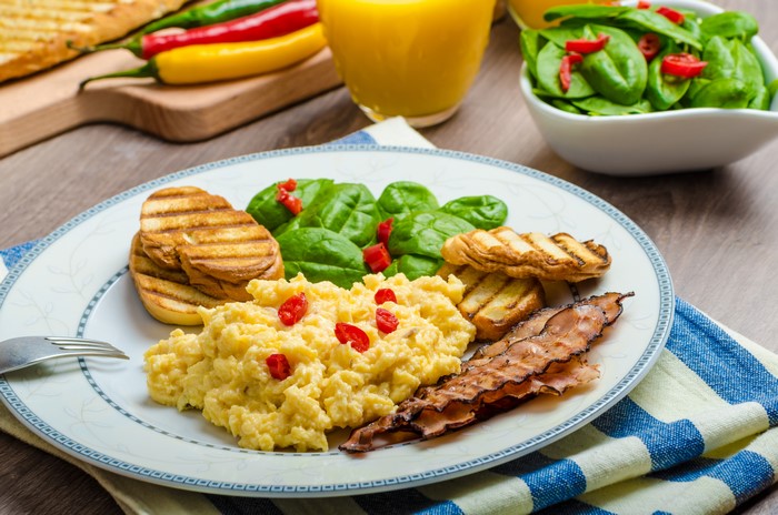 Scrambled eggs with bacon, toast, and spinach salad