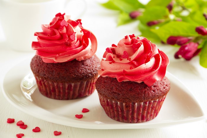 Two red velvet cupcakes with pink frosting and heart sprinkles