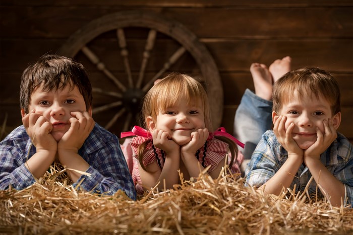 Three children lying on straw in front of a wooden wall