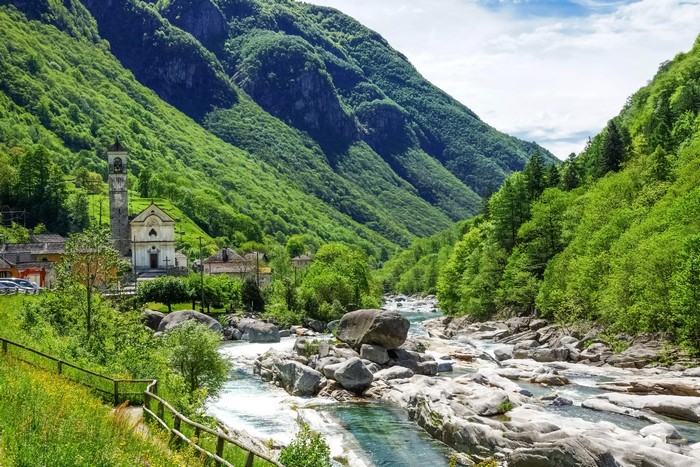 Village with church and bell tower by a rocky river in the Swiss Alps