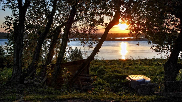 Sunset over a river with trees and a boat