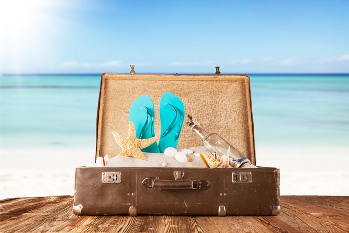 Suitcase with flip-flops and starfish on beach